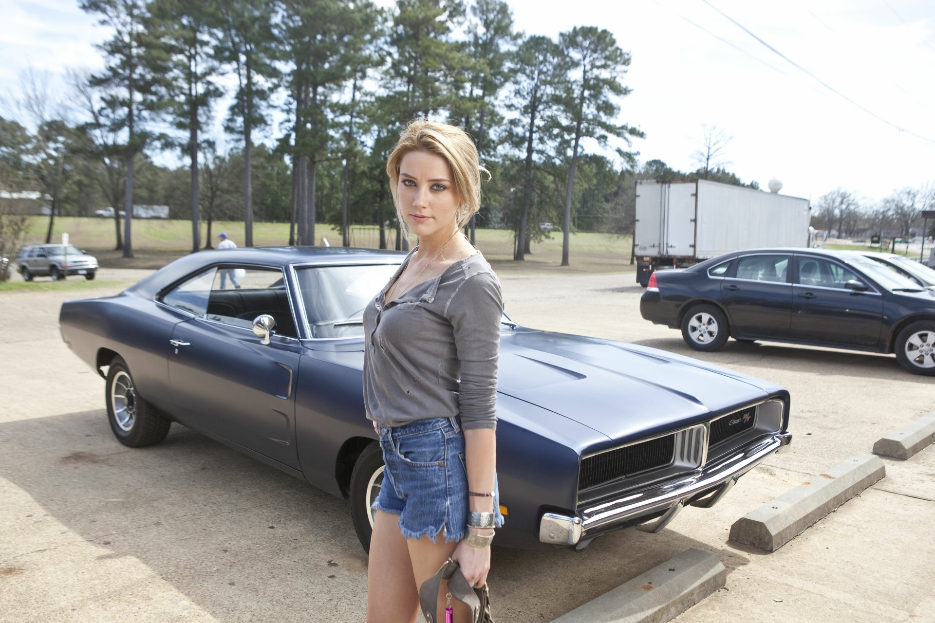 Amber Heard stands confidently beside a classic muscle car in a clear, outdoor setting, captured in a sharp 4K Ultra HD PC desktop wallpaper.