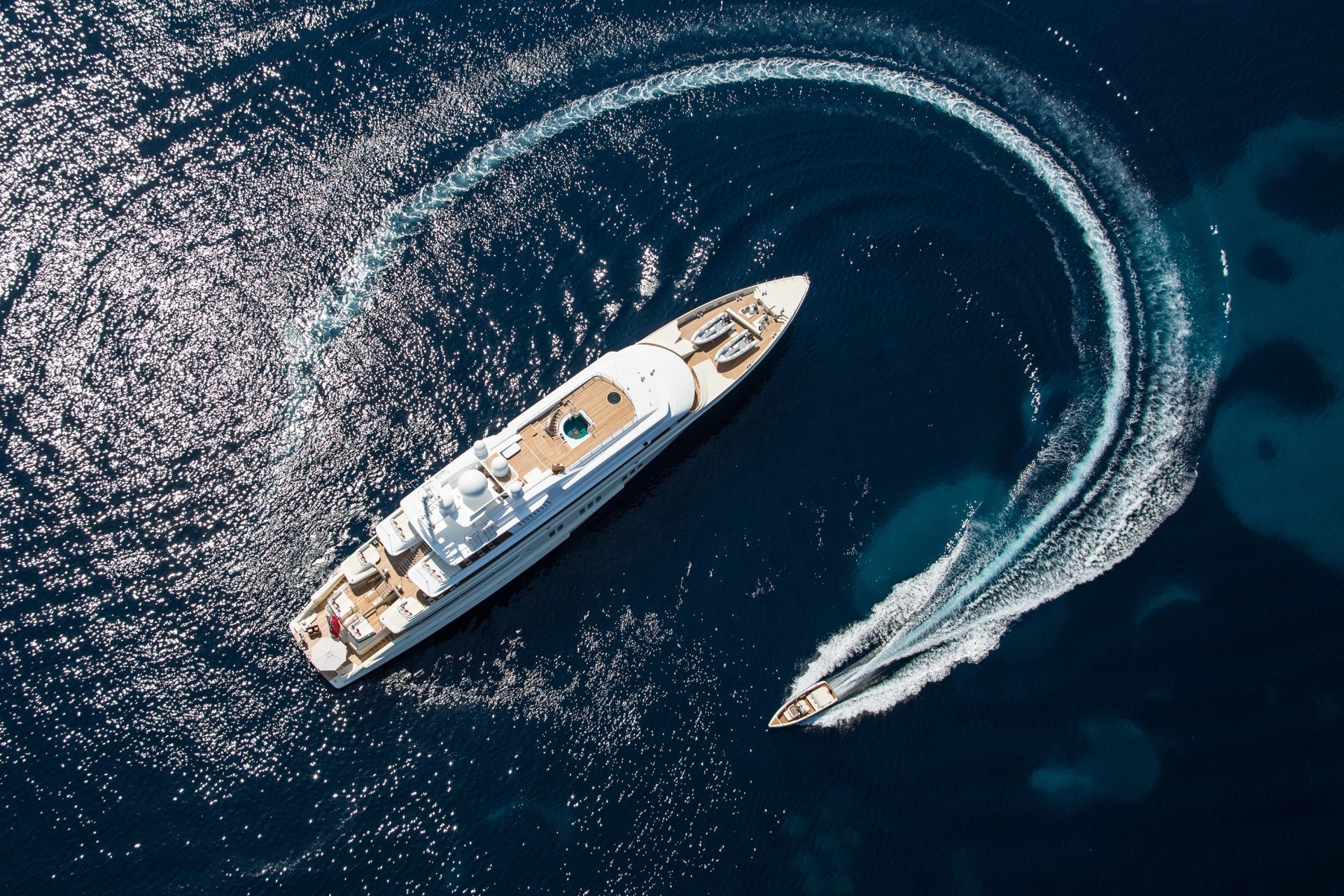 Aerial view of a yacht and a speedboat creating circular waves on deep blue water, captured in an HD PC desktop wallpaper featuring a ship and vehicle.