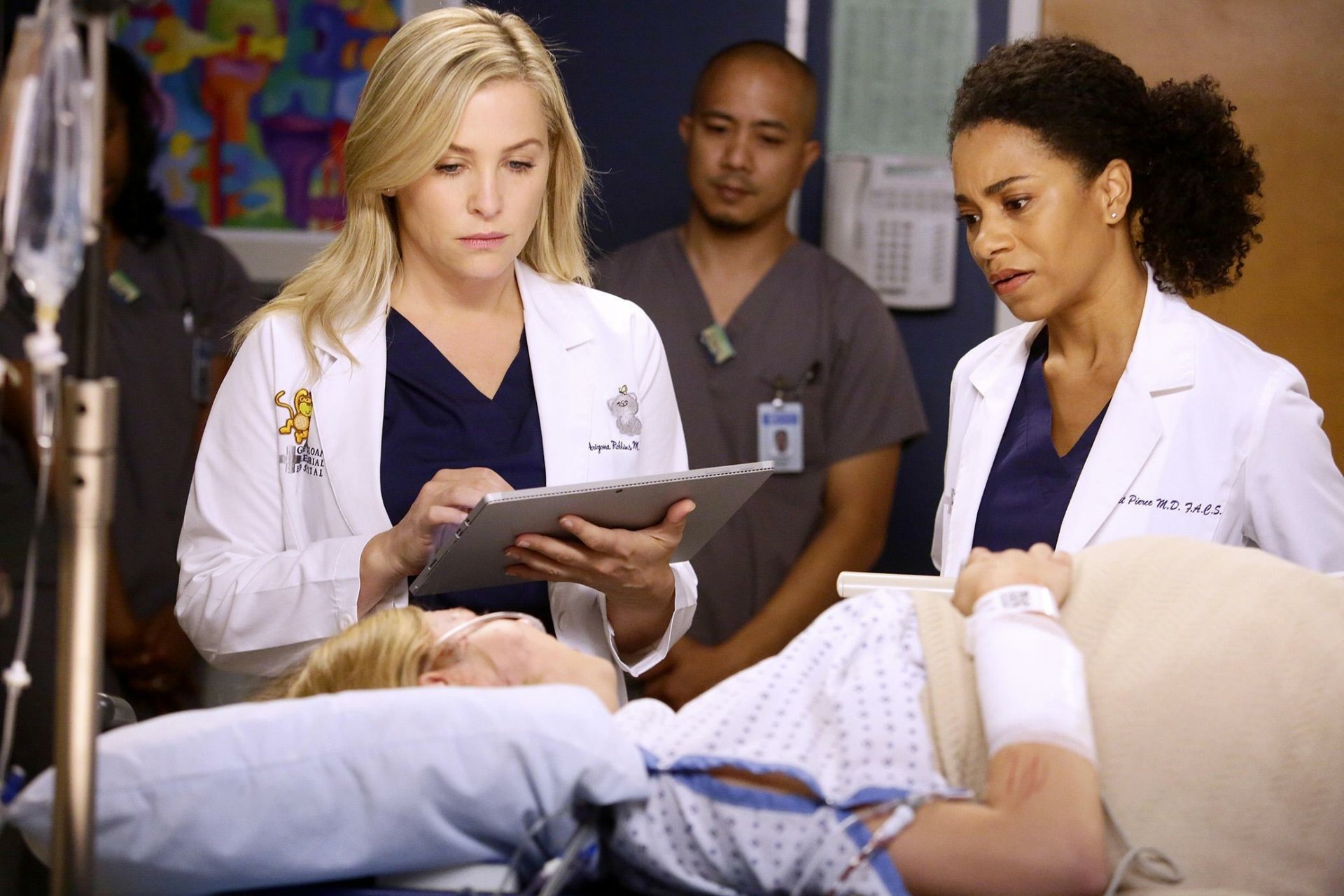 HD desktop wallpaper from Grey's Anatomy featuring two doctors consulting over a tablet beside a patient's bed.