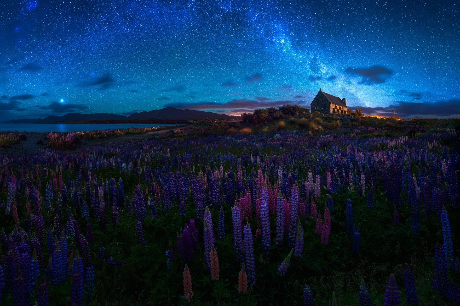 HD PC wallpaper: a small religious chapel under a starry night sky and Milky Way, foreground carpeted with purple lupine flowers.