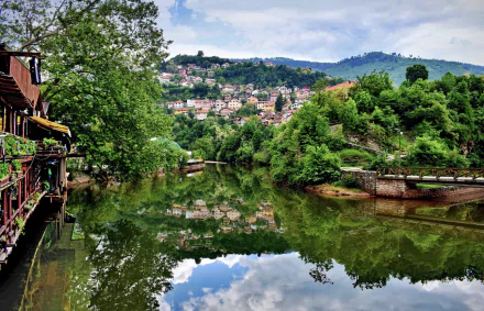 HD desktop wallpaper featuring a serene reflection of Sarajevo’s lush greenery and houses in a calm river, captured beautifully in vibrant photography.