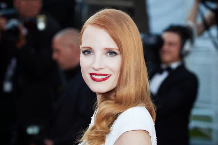 HD desktop wallpaper featuring American actress Jessica Chastain with red hair, blue eyes, red lipstick, and a bright smile at a formal event.