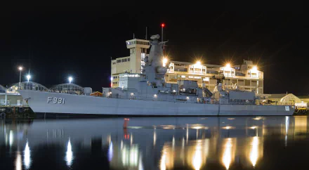 Night view of the Belgian frigate Louise-Marie (F931) docked, with lights reflecting on calm water, captured in high definition for a military-themed desktop wallpaper.