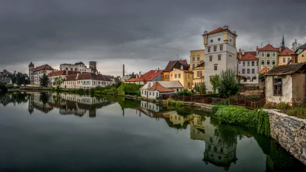 8K Ultra HD desktop wallpaper featuring a serene man-made lake reflecting the charming buildings of a historic town under a cloudy sky.