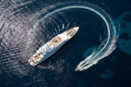 Aerial view of a yacht and a speedboat creating circular waves on deep blue water, captured in an HD PC desktop wallpaper featuring a ship and vehicle.