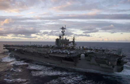 HD desktop wallpaper showing the USS John C. Stennis (CVN-74) aircraft carrier sailing under a cloudy sky in a military naval setting.