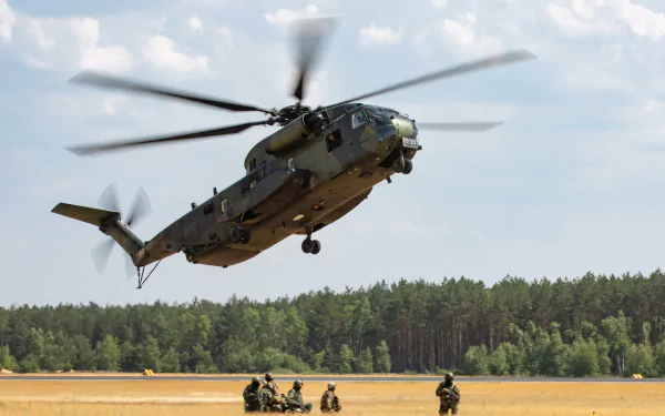 A military Sikorsky CH-53 Sea Stallion transport helicopter lifts off from a field with soldiers below, set against a forest and cloudy sky, captured as an HD desktop wallpaper.