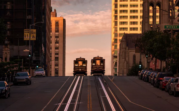 Two trams travel along a road lined with parked vehicles and tall buildings in San Francisco during sunset, captured in an HD PC desktop wallpaper.