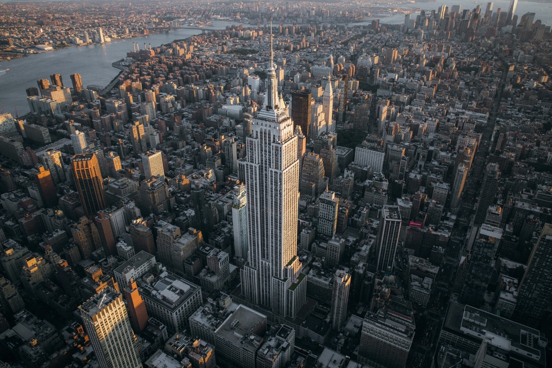 Aerial view of New York City featuring the Empire State Building towering over surrounding skyscrapers and cityscape at sunset.