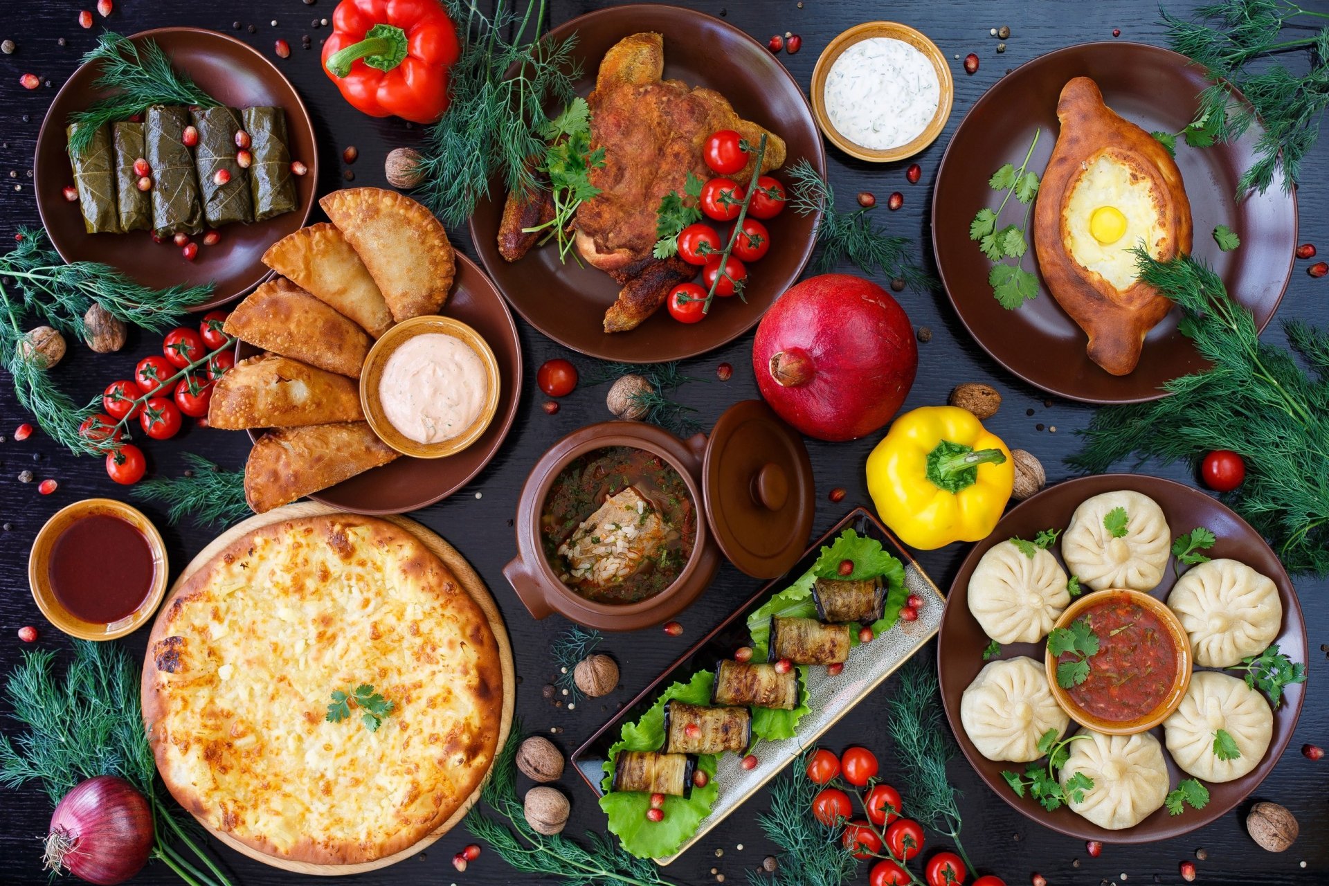 2K Quad HD PC desktop wallpaper: vibrant still-life spread of peppers, meat, tomatoes and assorted dishes—dumplings, skewers, cheese pie and sauces on rustic plates.