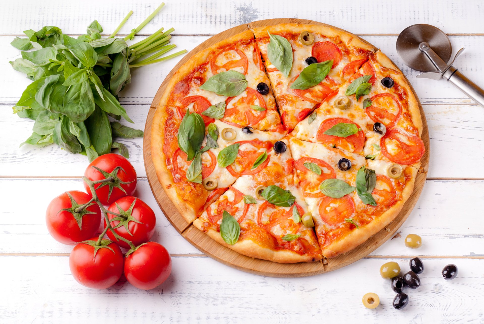 Still life HD PC desktop wallpaper/background: wood table with pizza topped with olives, tomato slices and basil; vine tomatoes and basil bunch alongside — appetizing food scene.
