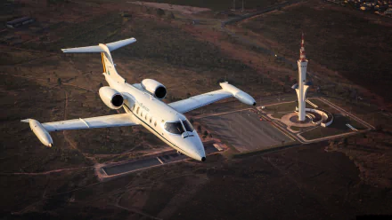 A Learjet 35 jet airplane flying above an expansive landscape near a distinctive tower, presented as an HD PC desktop wallpaper and background.