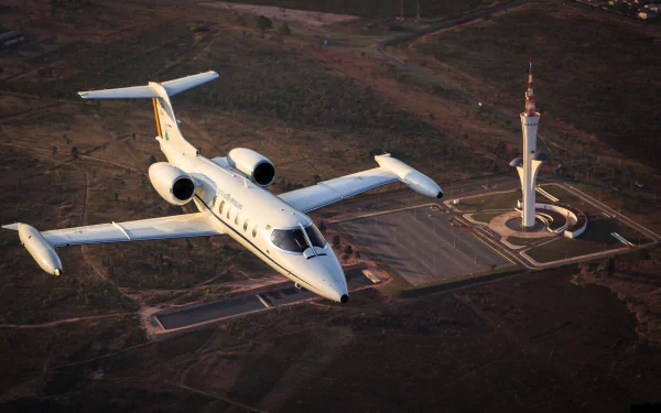 A Learjet 35 jet airplane flying above an expansive landscape near a distinctive tower, presented as an HD PC desktop wallpaper and background.