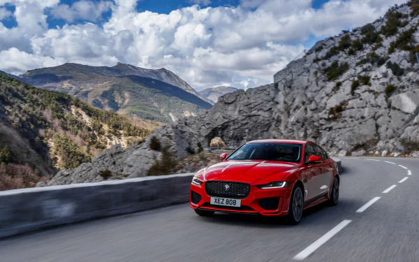 A red Jaguar XE car driving on a mountain road under a partly cloudy sky, showcased as a 4K Ultra HD PC desktop wallpaper and background.