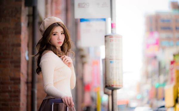 A 4K Ultra HD image of an Asian brunette woman wearing a hat, captured with a shallow depth of field, creating a soft cityscape background.
