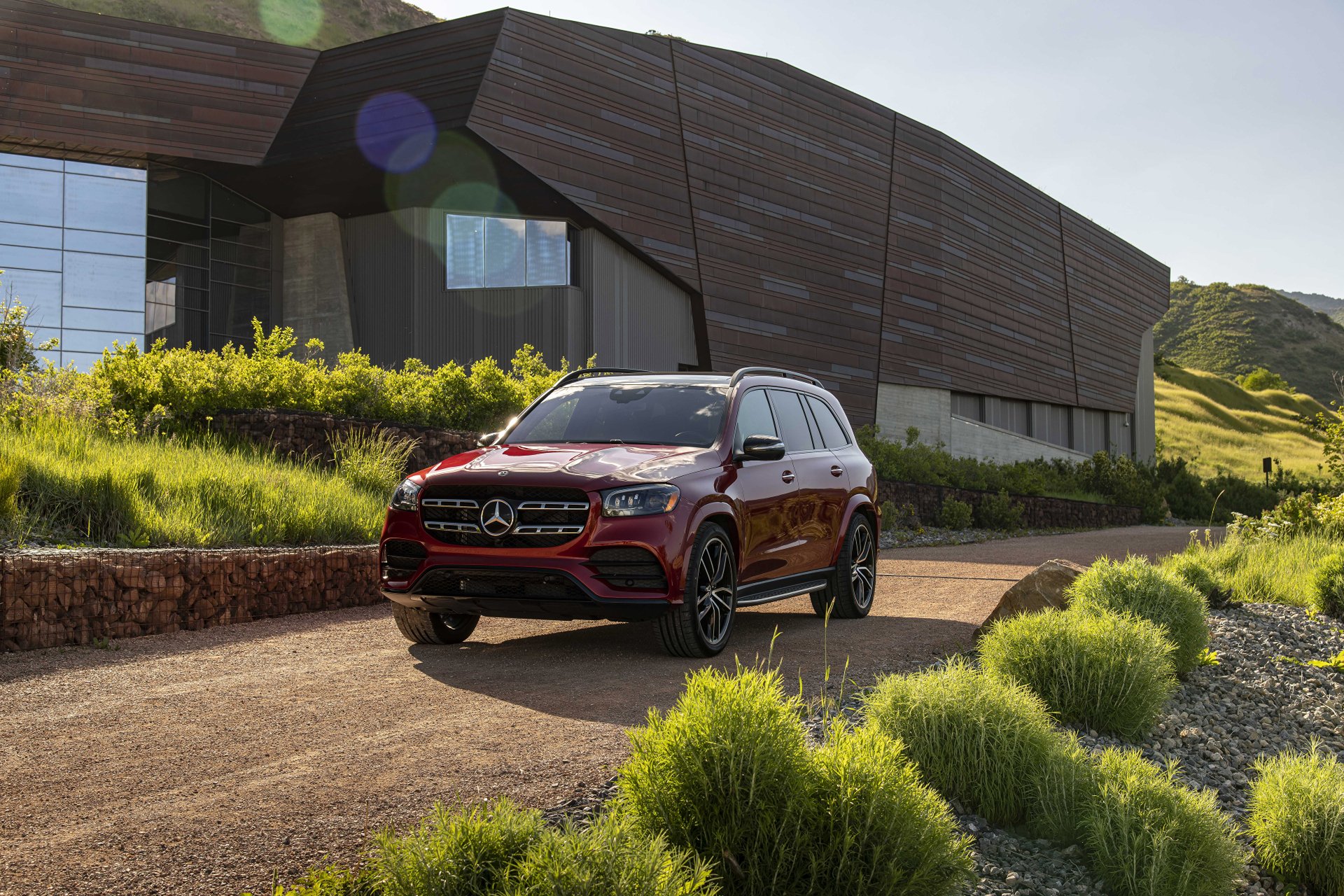 Red Mercedes‑Benz GL‑Class SUV parked on a gravel drive by a modern building and green hillside — 4K Ultra HD PC desktop wallpaper.