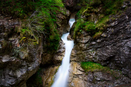 A stunning HD desktop wallpaper featuring a serene stream flowing through a rocky canyon, surrounded by lush green vegetation, embodying the tranquility of nature.