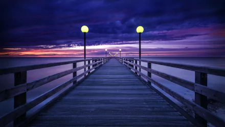 HD desktop wallpaper showing a man-made pier extending into the horizon under a purple sunset sky, illuminated by lampposts.