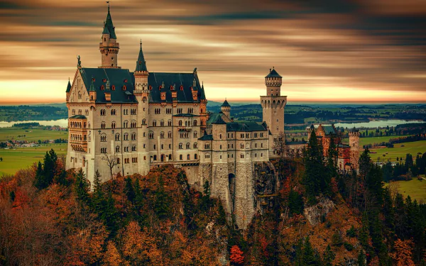 HD desktop wallpaper featuring the man-made Neuschwanstein Castle, with its majestic towers and spires, perched on a hilltop against a dramatic sky. Scenic landscape surrounds the iconic structure.