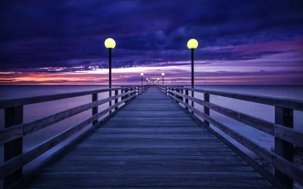 HD desktop wallpaper showing a man-made pier extending into the horizon under a purple sunset sky, illuminated by lampposts.
