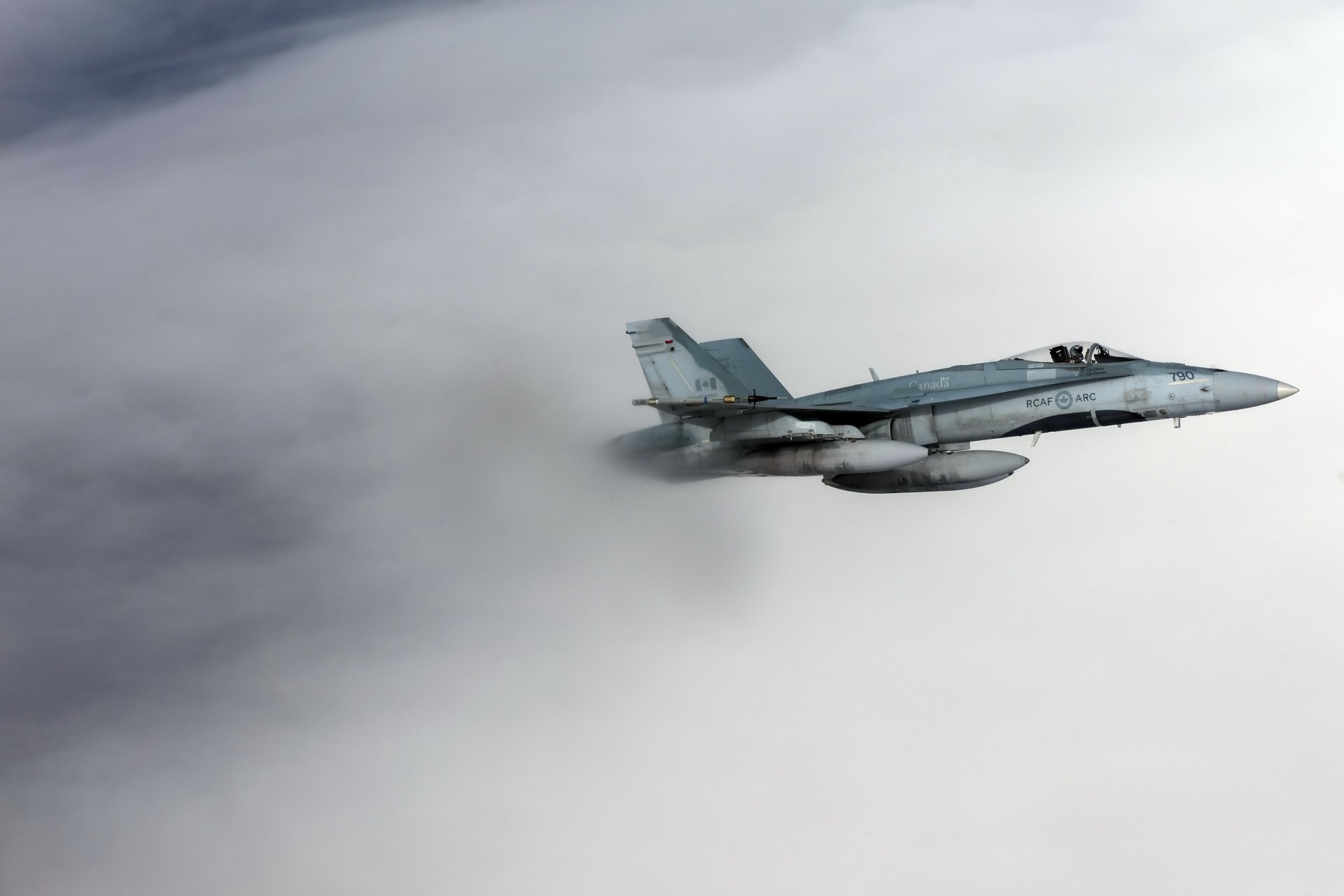 HD desktop wallpaper featuring a McDonnell Douglas CF-18 Hornet jet fighter soaring through cloudy skies in military flight.