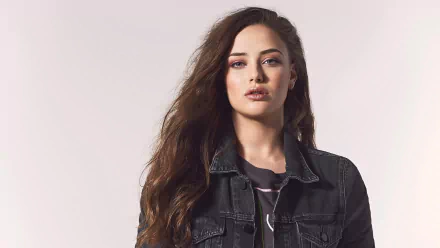 HD desktop wallpaper featuring Australian actress Katherine Langford with long brunette hair wearing a black denim jacket against a light background.