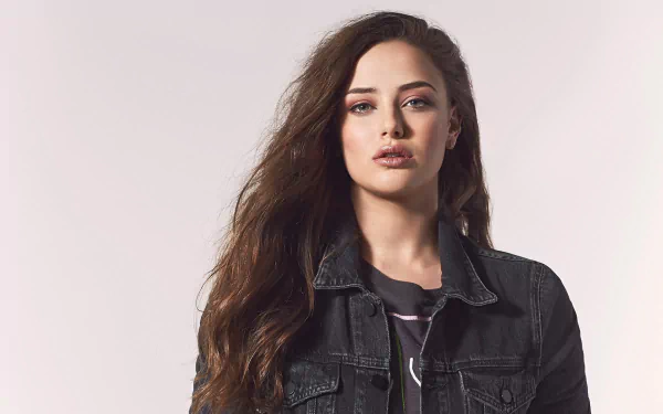 HD desktop wallpaper featuring Australian actress Katherine Langford with long brunette hair wearing a black denim jacket against a light background.
