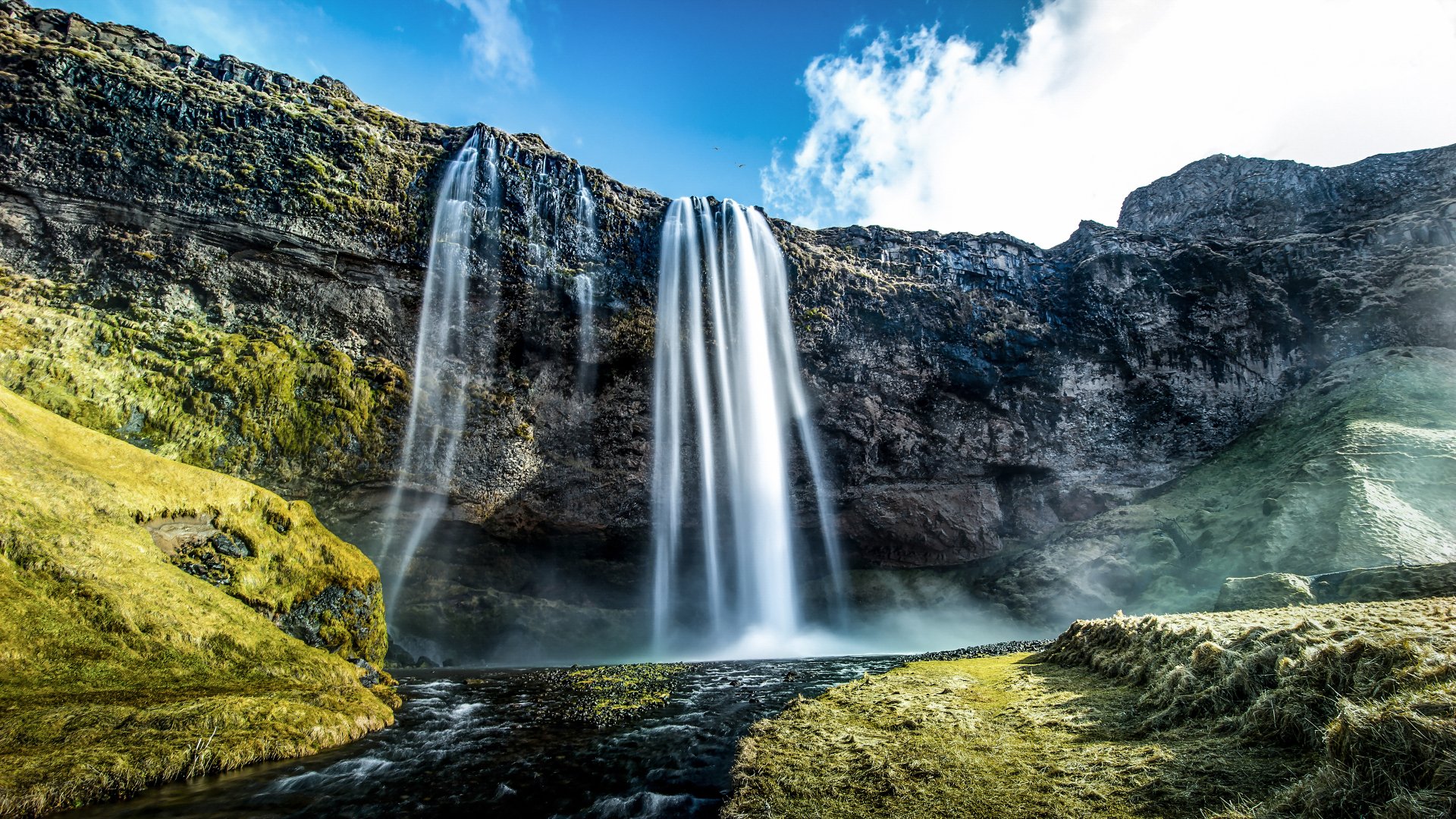 4K Ultra HD PC desktop wallpaper and background: Seljalandsfoss waterfall nature scene — towering white cascades over mossy cliffs, misty pool and green landscape under a vivid blue sky.