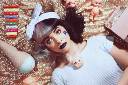 HD desktop wallpaper of American singer Melanie Martinez with bold lipstick, lying on a glittery surface surrounded by quirky dolls and colorful makeup items.