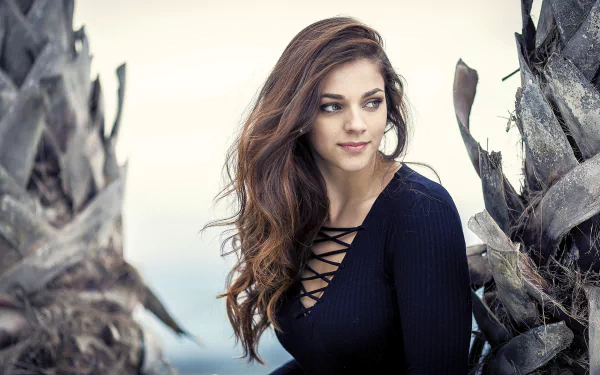 Brunette woman model with long flowing hair in a navy lace-up top, posed between weathered palm trunks — 4K Ultra HD PC desktop wallpaper and background.