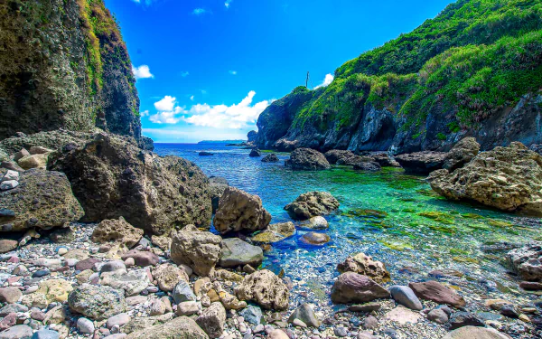 4K Ultra HD PC desktop wallpaper featuring a vibrant nature scene of a rocky beach with clear turquoise water and lush green cliffs under a bright blue sky.