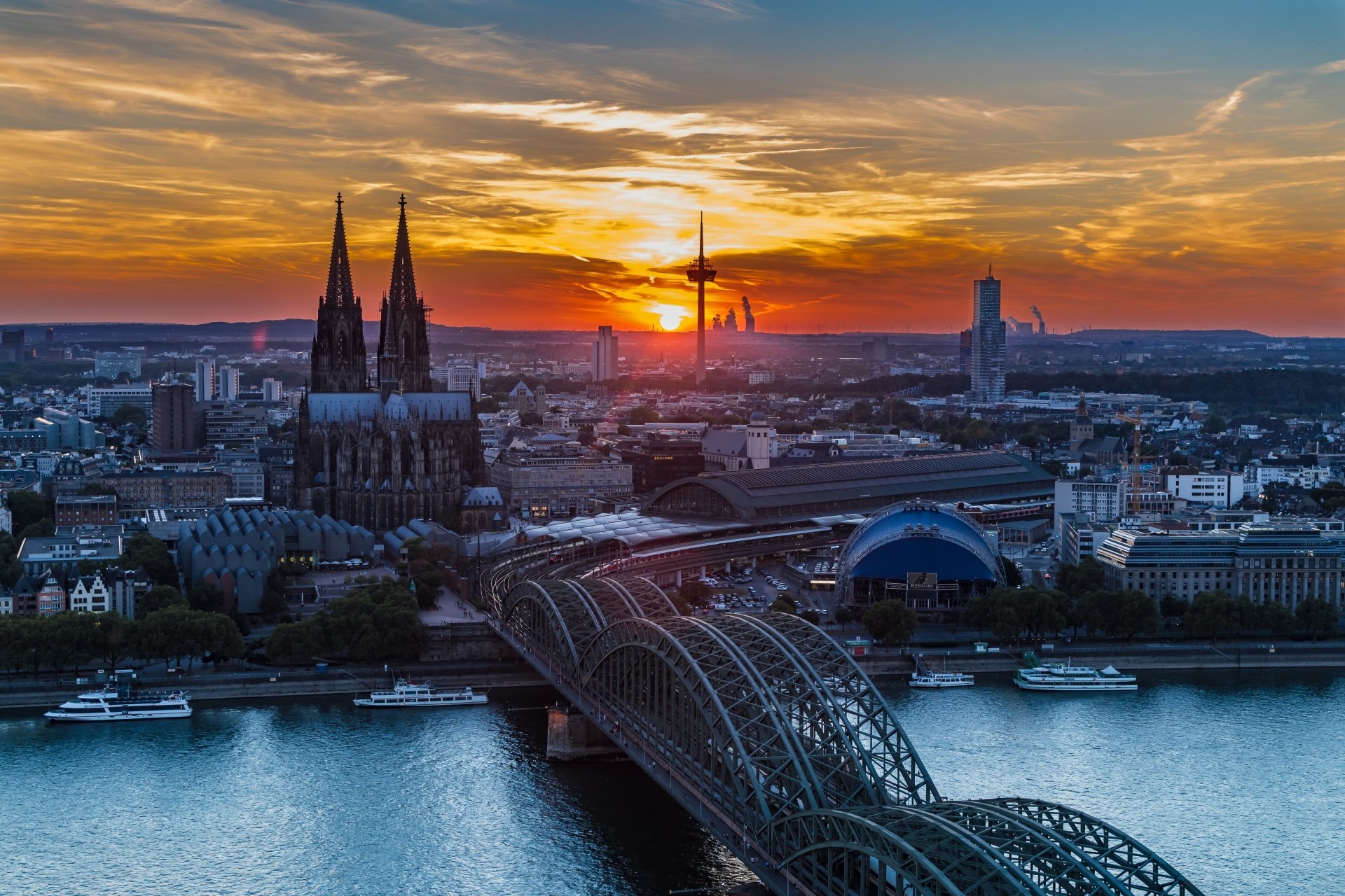 Sunset over the Hohenzollern Bridge crossing the Rhine River in Cologne, Germany, showcasing the city skyline in vibrant 4K Ultra HD detail.