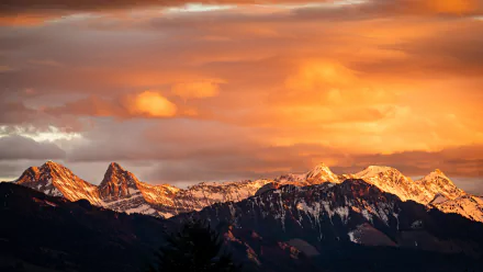 Snow-covered mountain range bathed in warm orange light under a dramatic sky, captured in stunning 4K Ultra HD quality for a nature-inspired desktop background.