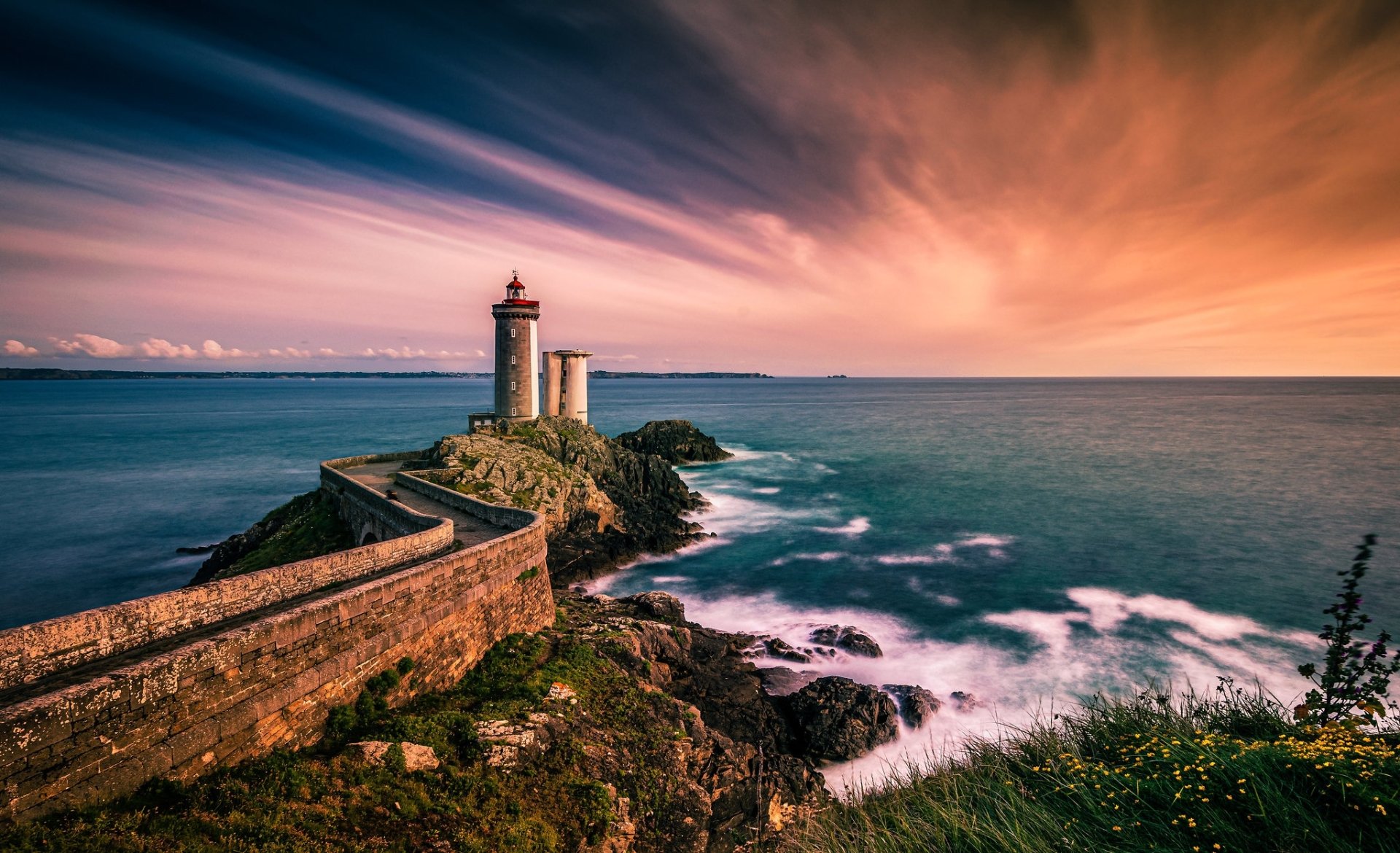 HD PC desktop wallpaper: French coastal, man-made lighthouse at sunset — stone path along the rugged coast to the ocean horizon.