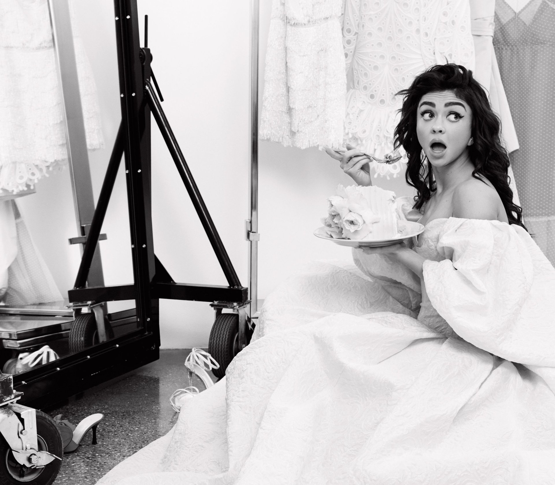 Black-and-white HD desktop wallpaper of a woman in an off-shoulder dress, seated in a dressing room holding a plate of cake with a surprised expression.