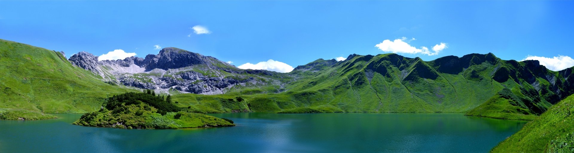 2K Quad HD PC desktop wallpaper: tranquil mountain lake scene — emerald slopes and rocky peaks reflected in still water beneath a clear blue sky.