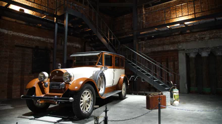 8K Ultra HD image of a 1923 Hudson Super Six 7-passenger vehicle displayed indoors, showcasing its vintage design with white and orange accents against an industrial backdrop.