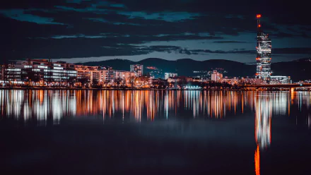 4K Ultra HD PC desktop wallpaper — Vienna night cityscape: illuminated modern buildings and a tall tower mirrored in calm river waters, a crisp man-made skyline beneath a deep night sky.