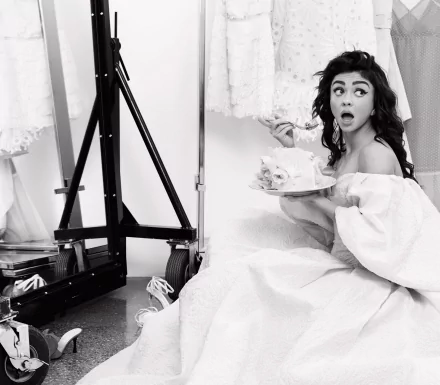 Black-and-white HD desktop wallpaper of a woman in an off-shoulder dress, seated in a dressing room holding a plate of cake with a surprised expression.