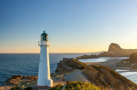 4K Ultra HD image of a man-made lighthouse on the New Zealand coast at horizon during sunset, featuring rugged cliffs and calm sea waters.