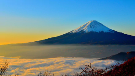 Snow-capped Mount Fuji rises above a blanket of clouds at sunrise, captured in vibrant 4K Ultra HD as a stunning nature mountain desktop wallpaper.