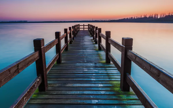 4K Ultra HD image of a wooden man-made pier extending into a calm lake at sunset, with soft pastel colors reflecting on the water.