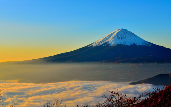 Snow-capped Mount Fuji rises above a blanket of clouds at sunrise, captured in vibrant 4K Ultra HD as a stunning nature mountain desktop wallpaper.