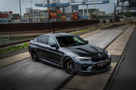 A silver BMW M5 car parked on industrial train tracks, captured in sharp 4K Ultra HD, showcasing the sleek design of this high-performance vehicle.