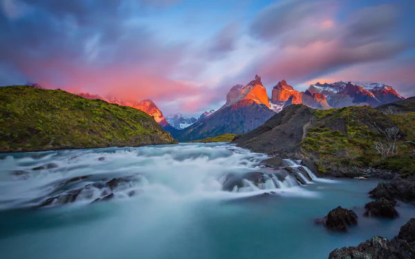 A vibrant HD desktop wallpaper of Torres del Paine National Park in Patagonia, Chile, showcasing a flowing river against dramatic mountain peaks at sunset.