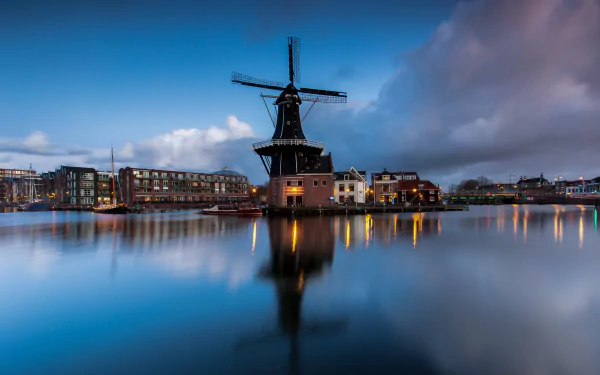 4K Ultra HD desktop wallpaper featuring a man-made windmill reflected in calm water with surrounding buildings under a dramatic evening sky.
