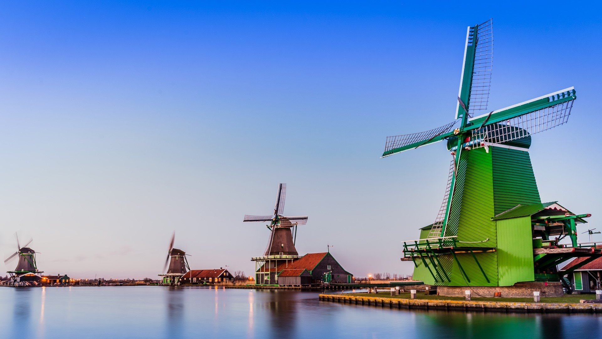 HD PC desktop background: Netherlands man-made windmills lining a calm waterfront at dusk, vivid sky and soft reflections.