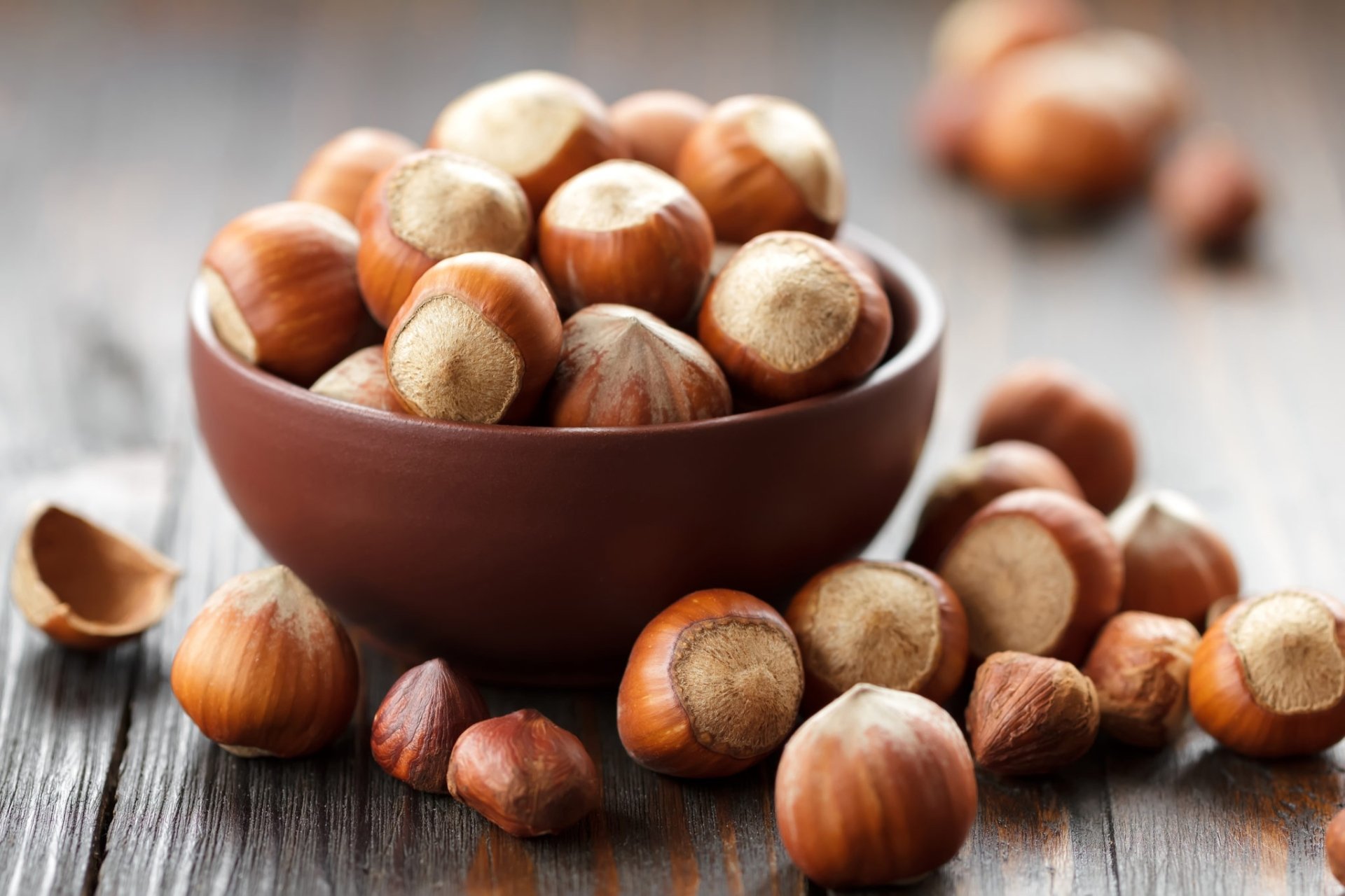 HD PC desktop wallpaper: close-up of whole hazelnuts in a brown bowl and scattered shells on a wooden surface, food-themed background.