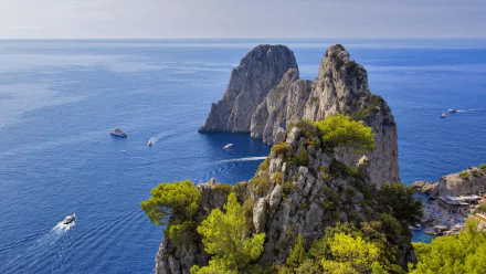 HD desktop wallpaper showing the Faraglioni rock formations rising from the blue sea off Capri, Italy, with a clear sky and horizon in the background.