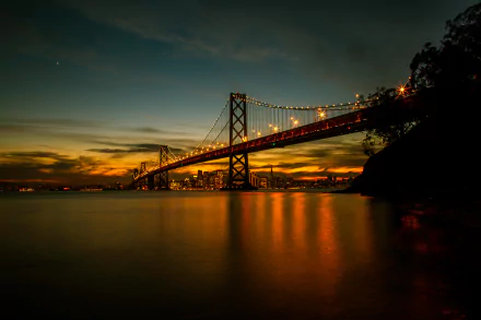 Sunset over San Francisco’s Bay Bridge in California, captured in stunning 4K Ultra HD with glowing lights reflecting on calm water.
